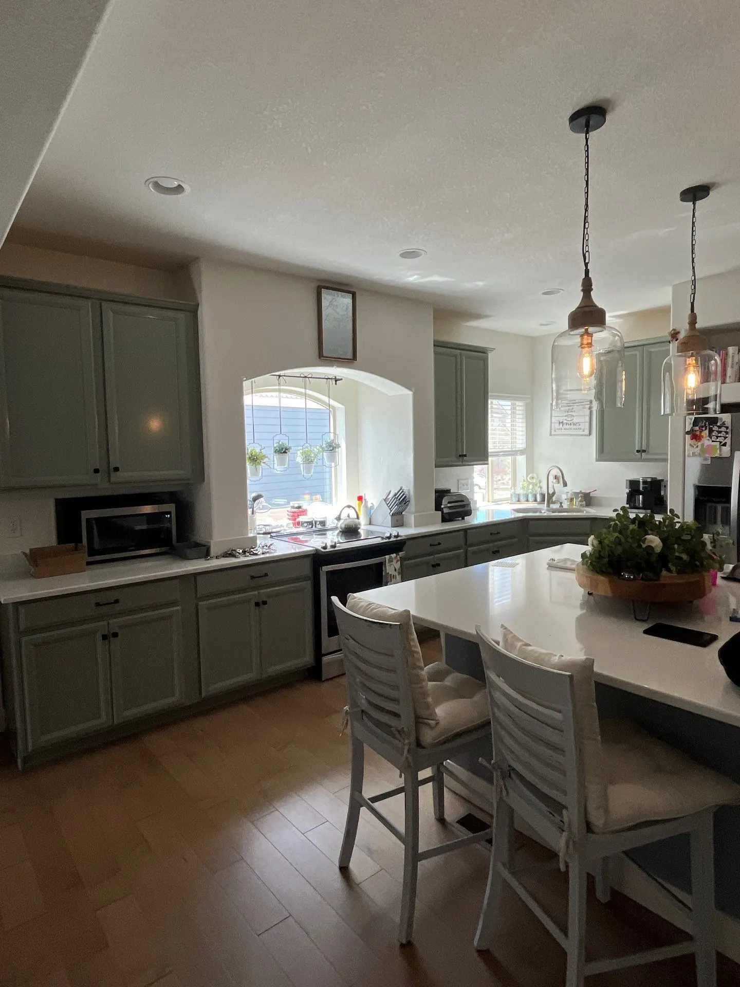 Repainted sage green kitchen cabinets around an island with pendant lighting